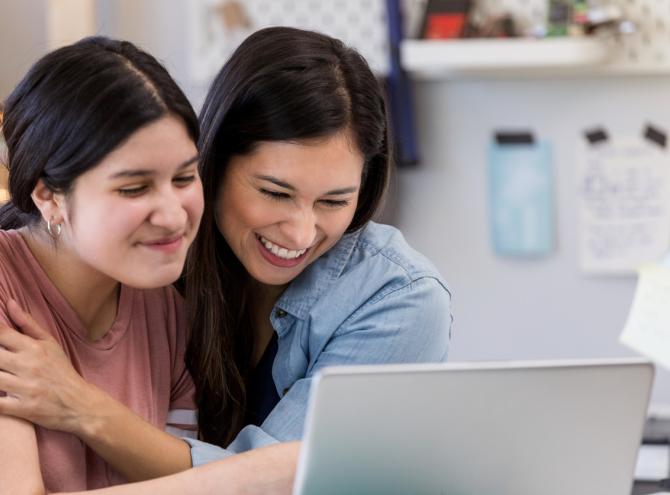Mother and daughter hugging while looking at computer screen